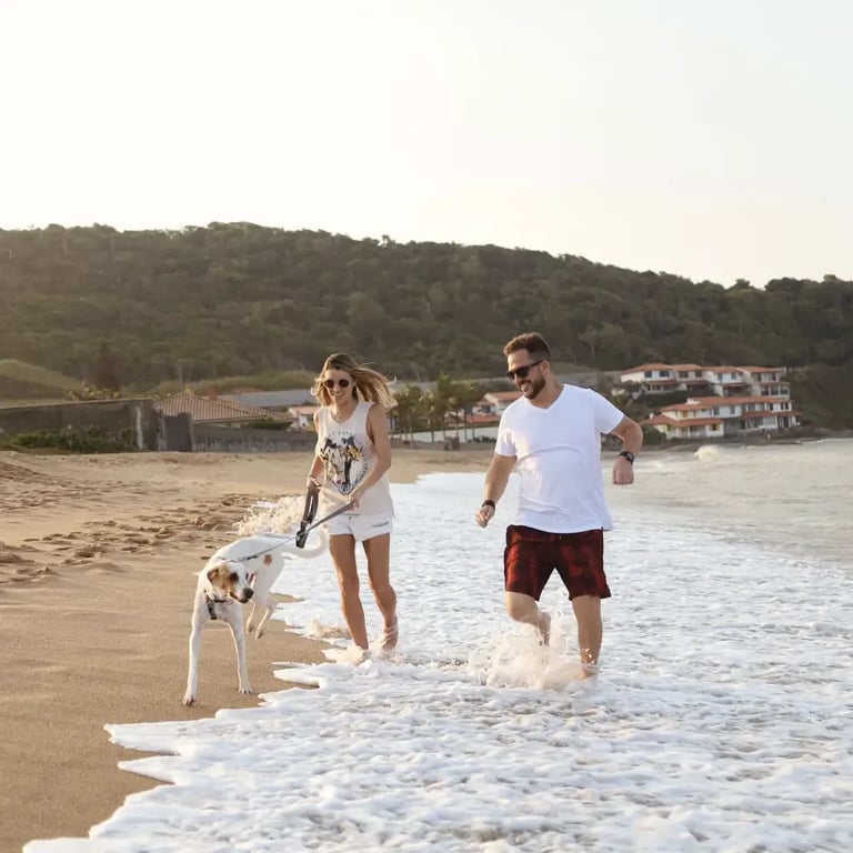 Casal caminhando com o cachorro na beira da Praia Rasa